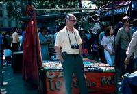 Herb Striner, with pipe and camera in an open air market in Paris, France