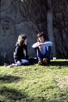 Young man and woman sitting on grass in front of stone wall