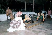 Dancers engaging in bamboo dance under thatched roof
